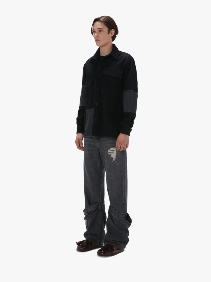 Model wearing a black button-up shirt and dark grey distressed jeans against a plain white background