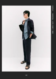 Man wearing dark jacket and linen trousers holding a black bag against a plain white background for Massimo Dutti