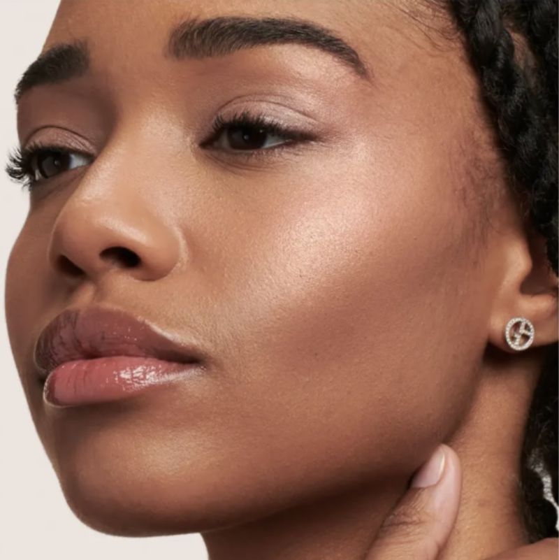 Close up of a woman's face showcasing her skin tone, light pink lip gloss and earring with a symbol on it.