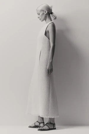 Model in profile wearing a textured cream dress and strappy flat sandals against a light grey studio background.