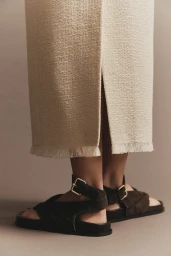Close-up of a person wearing black strappy sandals and a textured cream skirt with a front slit for A.Emery Resort Campaign 25.