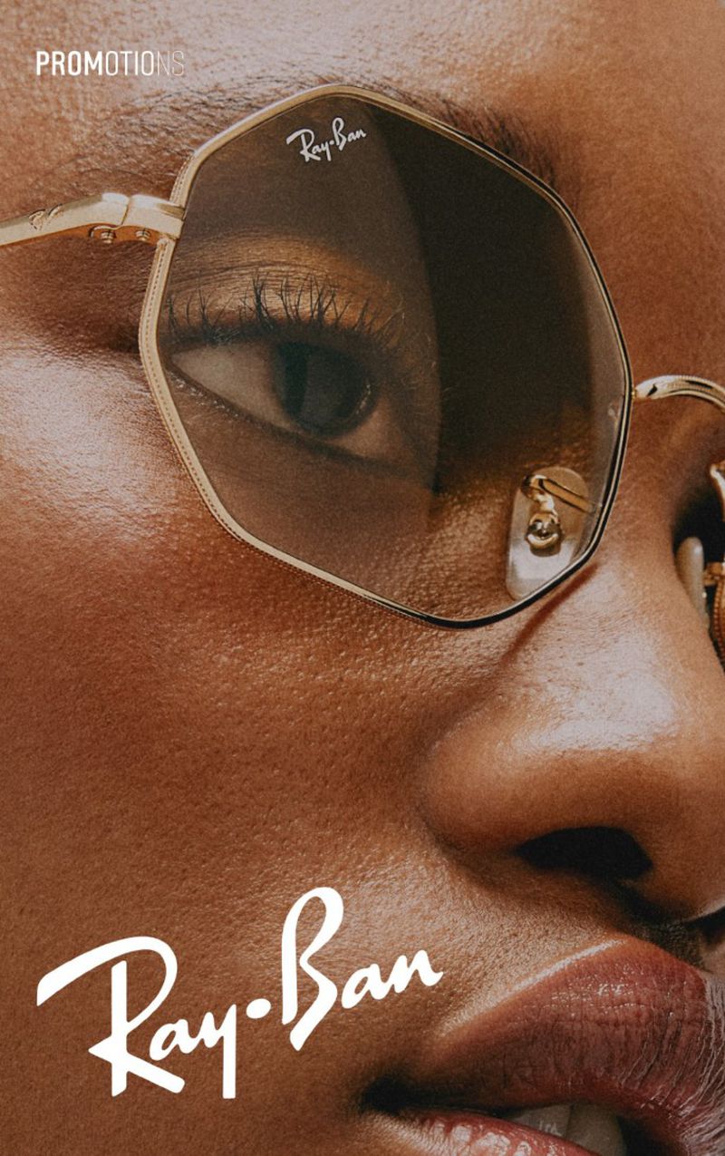 Close-up studio shot of an African-American woman wearing gold-framed Ray-Ban sunglasses, displaying the brand logo and product details.