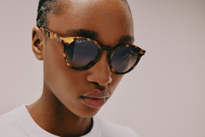 Close-up of an adult woman with dark skin and short hair, wearing patterned sunglasses, posing in front of a neutral background.