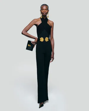 Model Debra Shaw in a black halter jumpsuit with gold hardware and earrings against a white seamless backdrop
