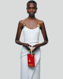 Model Debra Shaw wearing a white Schiaparelli dress holding a structured red handbag against a neutral grey background