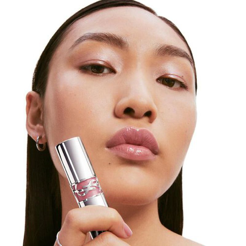 Close-up of a woman with fair skin holding a tube of lip gloss, showcasing its glossy texture and the effect on her lips.