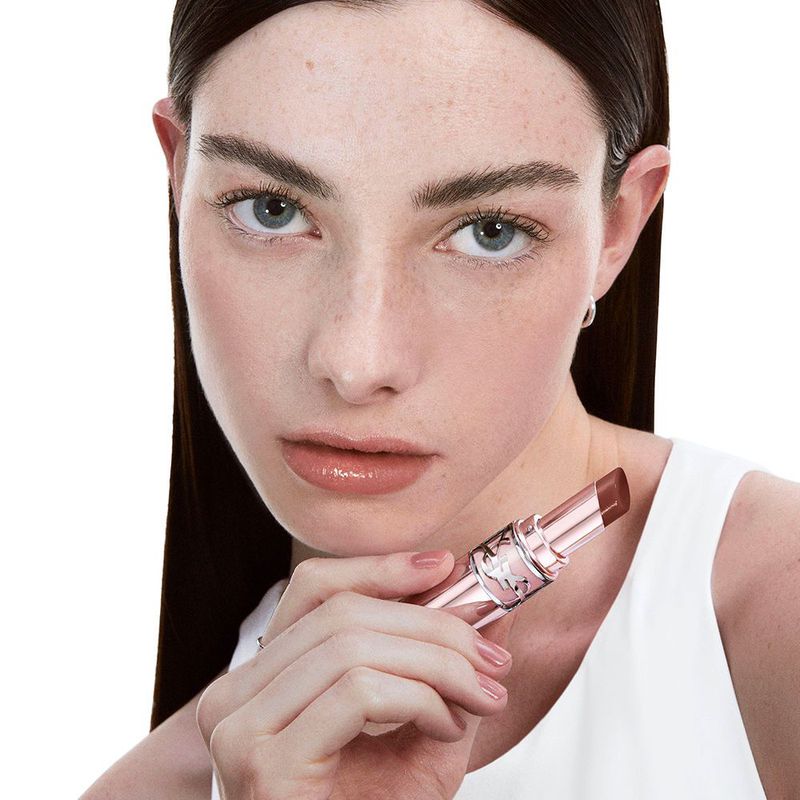 Close-up of a young adult female holding a tinted lip balm, showcasing its color and packaging against a white background.