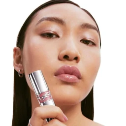 Close up beauty portrait of a model holding a silver YSL Loveshine lipstick near her glossy lips against a clean white background
