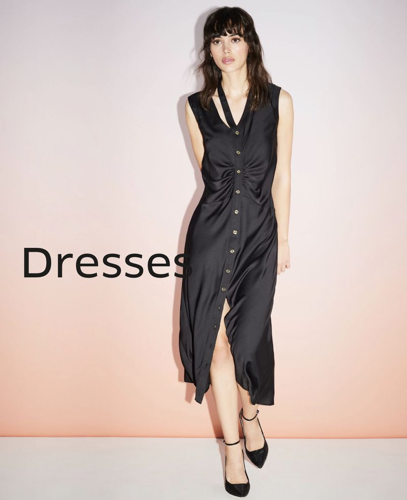A stylish woman poses in a black midi dress with button-up detailing and ankle-strap heels against a gradient background.