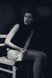 Model seated on a wooden chair wearing a dark sleeveless top against a dark background for H&M Swim S/S 24