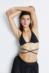 Model wearing a black bikini top with straps and dark bottoms posing against a plain white background.