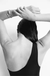 Close-up back view of a model in a black swimsuit wearing a silver cuff bracelet with arms raised.