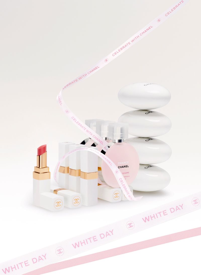 Still life of Chanel beauty products: lipstick, fragrance, soaps. White and gold cosmetics arranged with ribbon on a bright background.