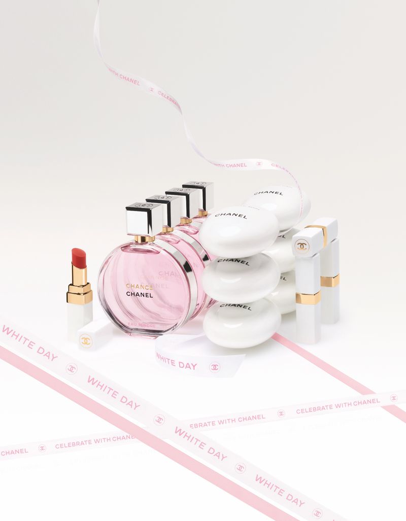 Chanel perfume bottles, soaps, and lipstick arranged on a white surface with decorative ribbons, showcasing beauty and luxury products.