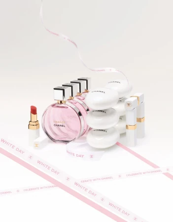 Chanel perfume bottles, soaps, and lipstick arranged on a white surface with decorative ribbons, showcasing beauty and luxury products.