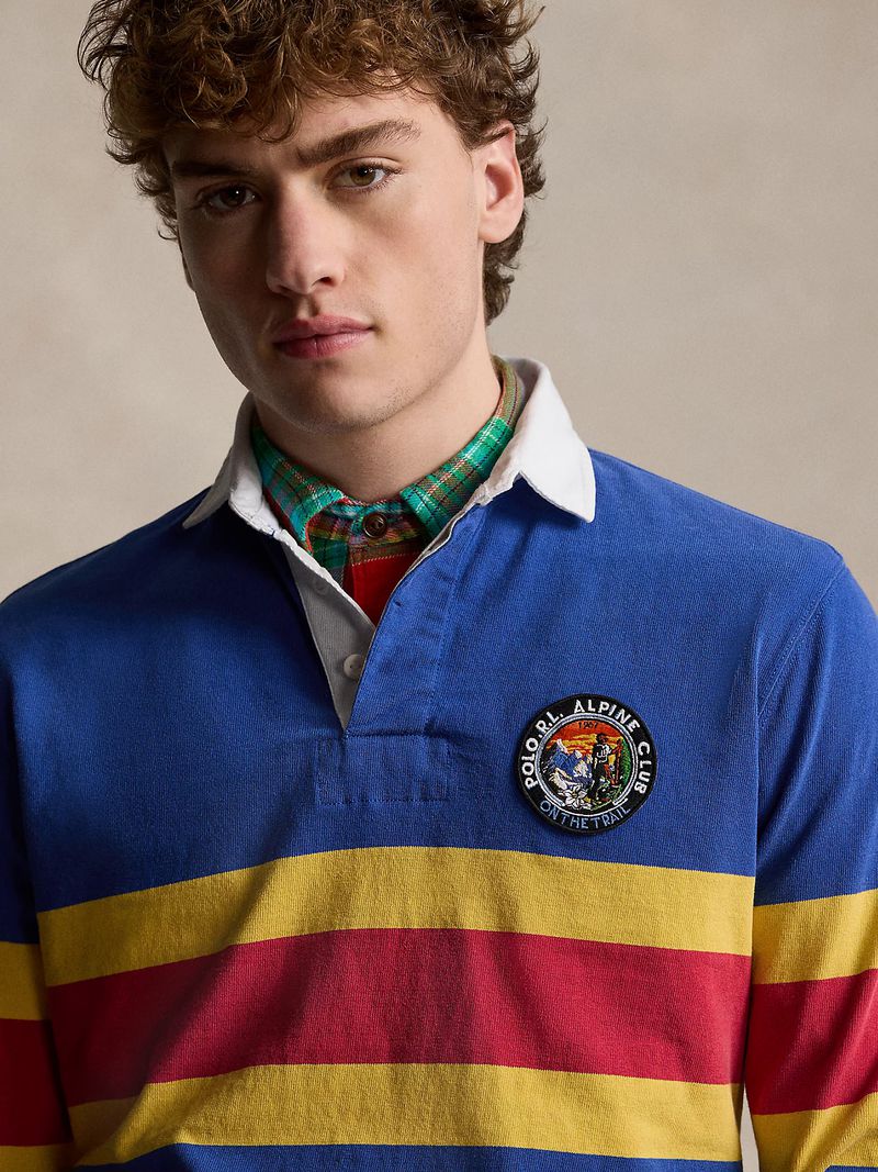 Adult male with curly brown hair wears a blue, yellow, and red striped rugby shirt with a Polo S.R.L. Alpine Club patch.