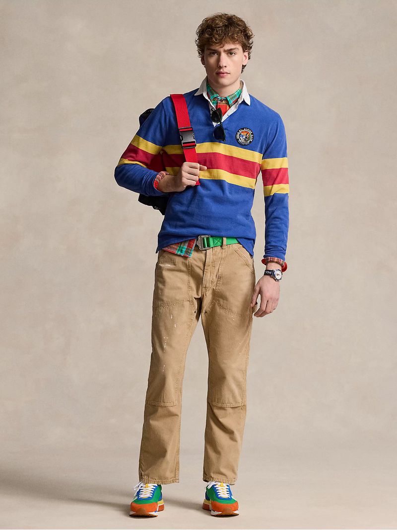 Young man poses in a blue striped rugby shirt, khaki pants, colorful sneakers, and a backpack in a studio shot for fashion.