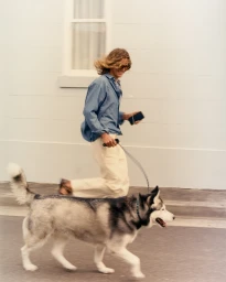 A long-haired person running along a sidewalk with a husky dog on a leash for Charlton Studio