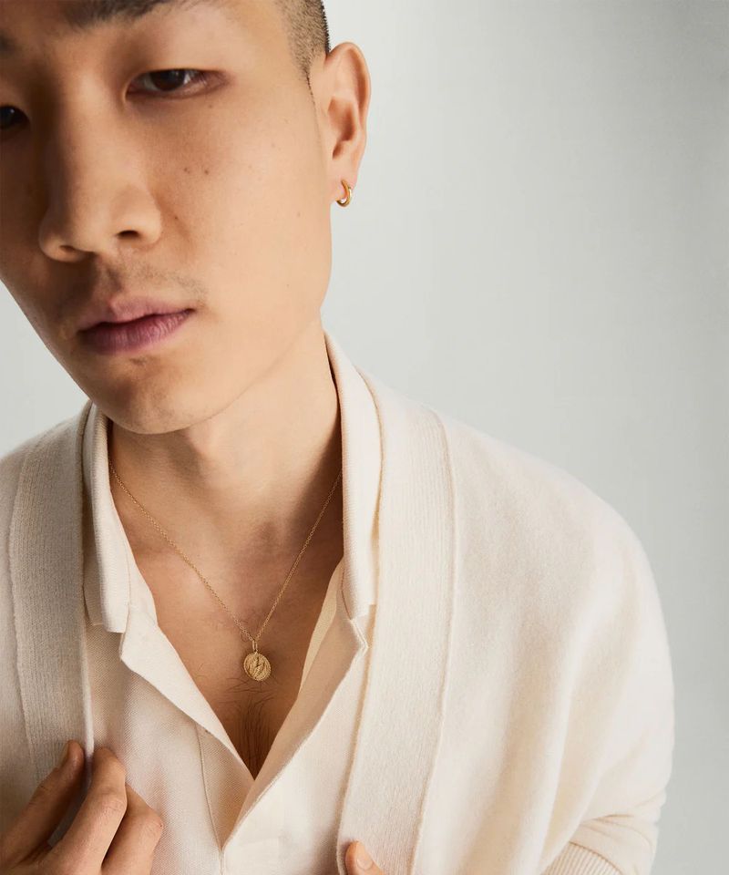 Close-up of an Asian adult male wearing a gold necklace and a light-colored sweater, set against a soft, neutral background.