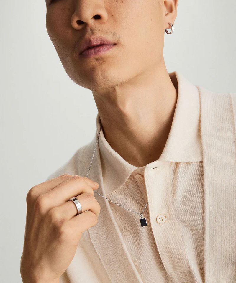 Portrait of a light-skinned man wearing a button-down shirt and silver pendant necklace; close-up shot in a neutral indoor setting.