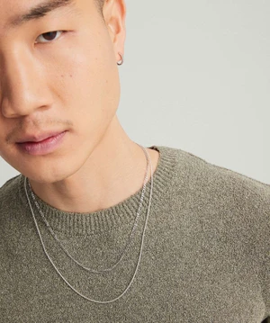 Close-up portrait of a man wearing layered silver chain necklaces and a hoop earring against a plain light background