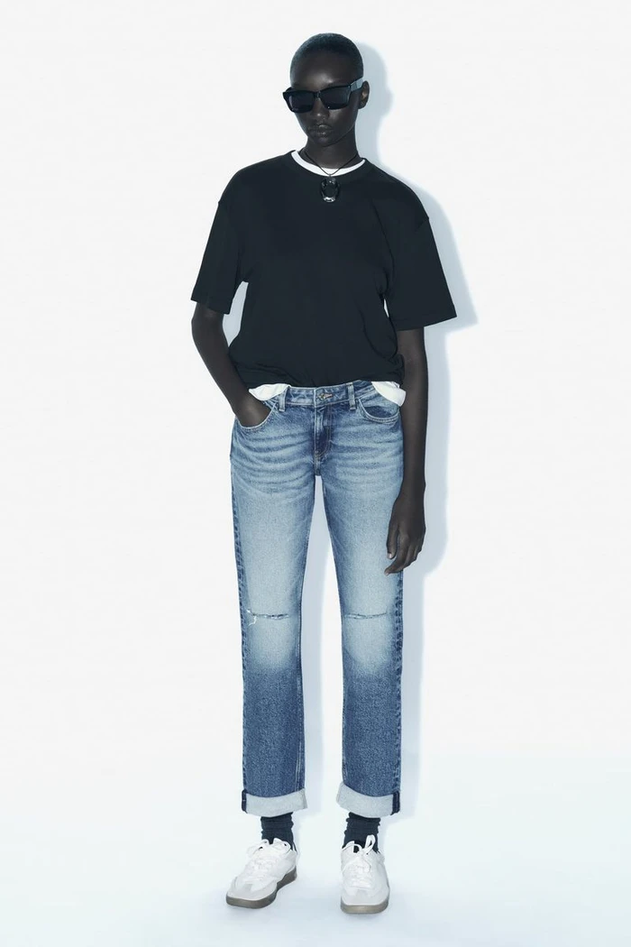Model in black t-shirt and blue denim jeans wearing sunglasses against a white background