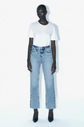 Model standing against a plain white background wearing a white t-shirt and blue denim jeans