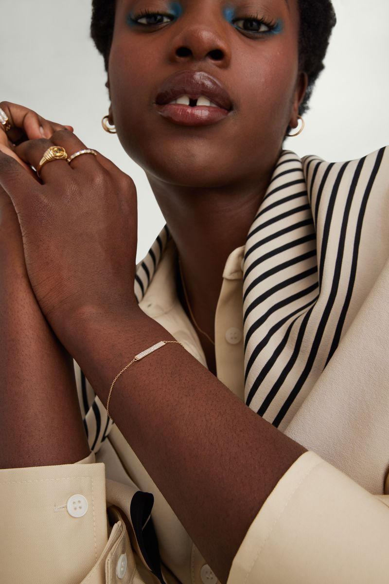 Portrait of a dark-skinned adult female wearing makeup and jewelry, with her hands and arms displayed in the foreground.