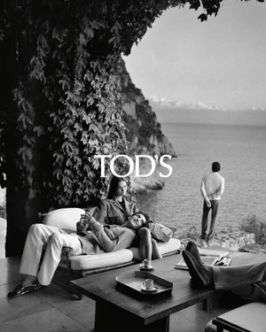 Black and white fashion campaign photograph featuring models lounging on a cliffside terrace overlooking the sea for Tod's.