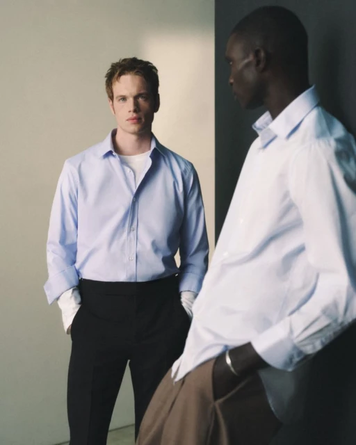 Two male models wearing light blue button-down shirts and tailored trousers for the Mr Porter Essentials Campaign studio shoot.