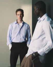 Two male models wearing light blue button-down shirts and tailored trousers for the Mr Porter Essentials Campaign studio shoot.