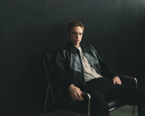 Man seated in a leather armchair wearing a black leather jacket against a dark wall for Mr Porter Essentials Campaign