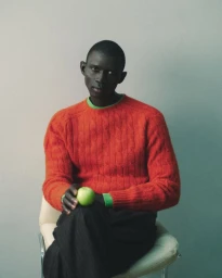 Fernando Cabral seated in an orange cable-knit sweater holding a green apple against a muted studio background.