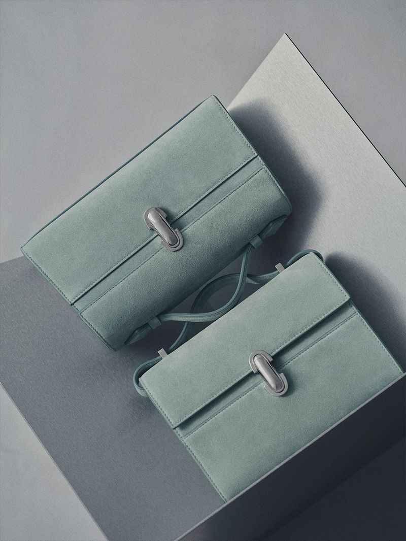 Two light-blue suede handbags with silver clasps on a geometric gray surface, showcasing a minimalist and fashionable aesthetic.