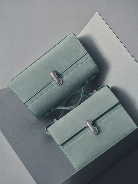 Two light-blue suede handbags with silver clasps on a geometric gray surface, showcasing a minimalist and fashionable aesthetic.