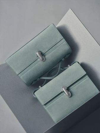 Two light-blue suede handbags with silver clasps on a geometric gray surface, showcasing a minimalist and fashionable aesthetic.