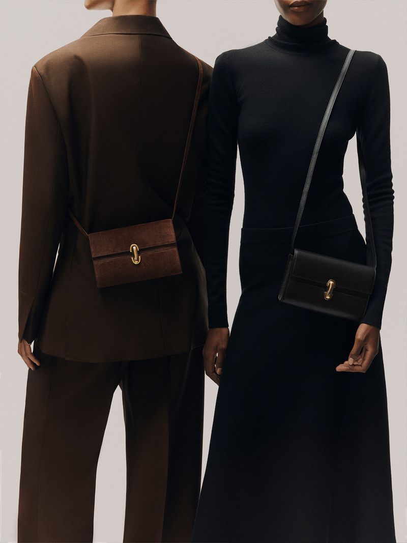Two models wearing tailored brown and black outfits, each wearing a small rectangular leather crossbody bag with a gold clasp.