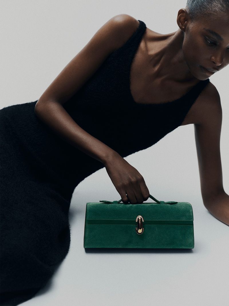 Elegant woman in a black dress poses with a green box handbag against a clean white backdrop, showcasing fashion and style.