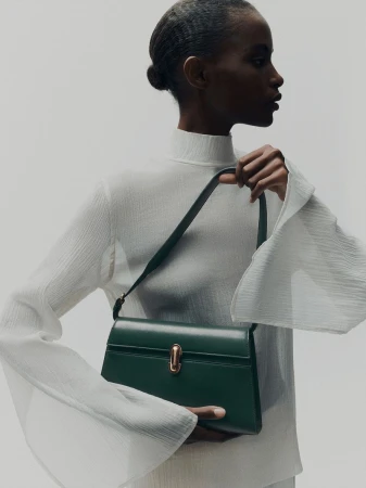 Elegant dark green leather satchel handbag displayed by a Black female model wearing a white top and neutral studio background.