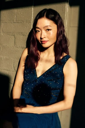 Figure skater Maia Shibutani posing in an embellished teal dress against a sunlit textured wall.