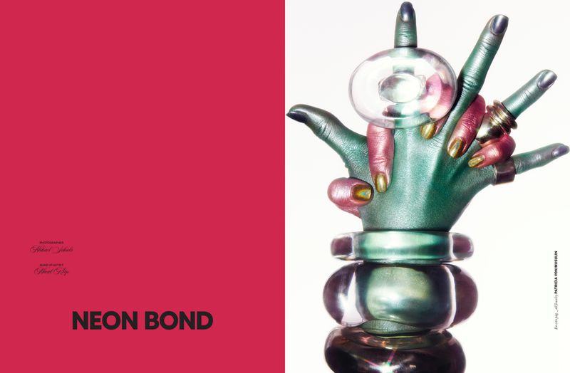 Fashion editorial featuring a hand sculpture with rings, bracelet, and a clear round orb against a contrasting bright pink background.