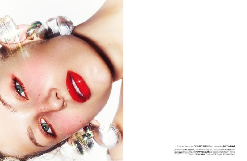 Glamorous beauty portrait of a model with bold red lips and reflective, rounded hair accessories against a clean, white backdrop.