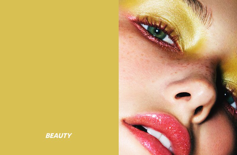 Close-up of a woman's face featuring vibrant yellow eyeshadow, pink lipstick, and flawless skin, set against a solid yellow background.