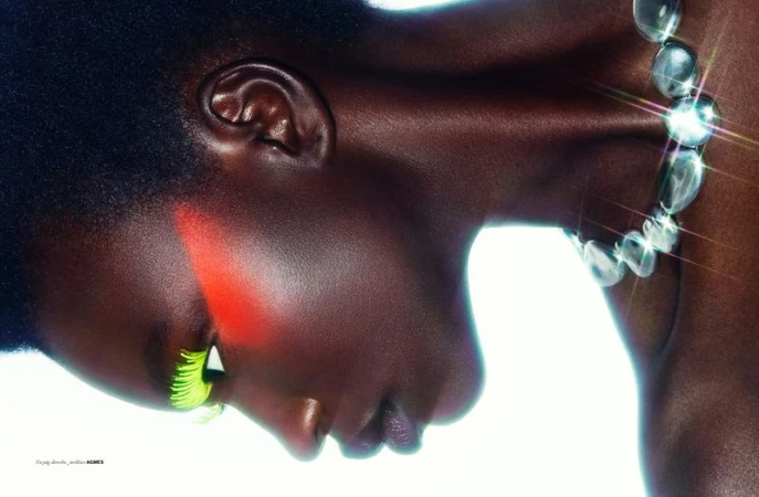 Close-up portrait of a Black female adult with bright makeup, wearing a light-colored crystal necklace against a bright white background.