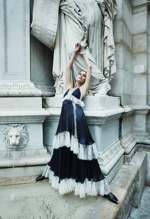 Model Anthi Fakidari in a black and white lace gown posing dramatically before classical stone architecture and a fountain.