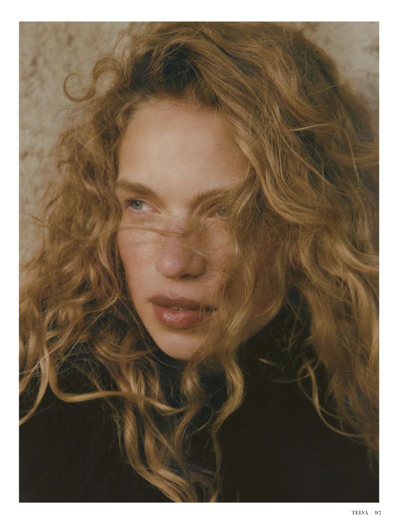 Portrait of a curly haired adult woman with fair skin wearing a dark turtle neck sweater against a neutral background.