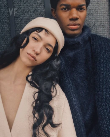 A young couple in stylish knitwear and neutral tones poses close together, capturing an intimate moment in a natural light setting.