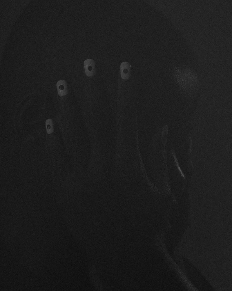 A person with pale, augmented eyes is seen in a dark environment, conveying an eerie and surreal visual, in a monochrome aesthetic.
