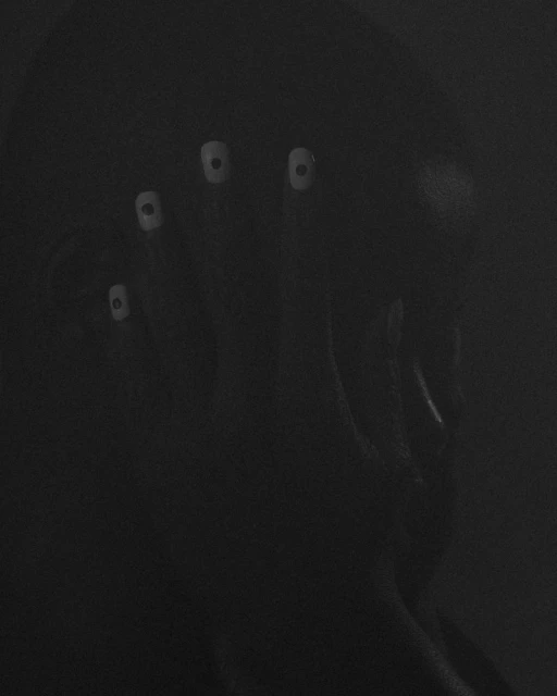 A person with pale, augmented eyes is seen in a dark environment, conveying an eerie and surreal visual, in a monochrome aesthetic.