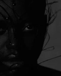 Monochrome close-up beauty portrait of a Black woman with delicate wire and bead face embellishments in low-key lighting.